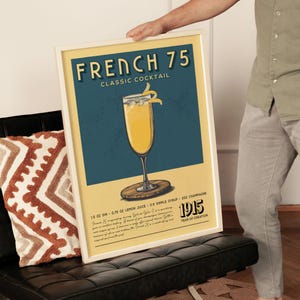A person is holding up a framed poster advertising a French 75 cocktail.