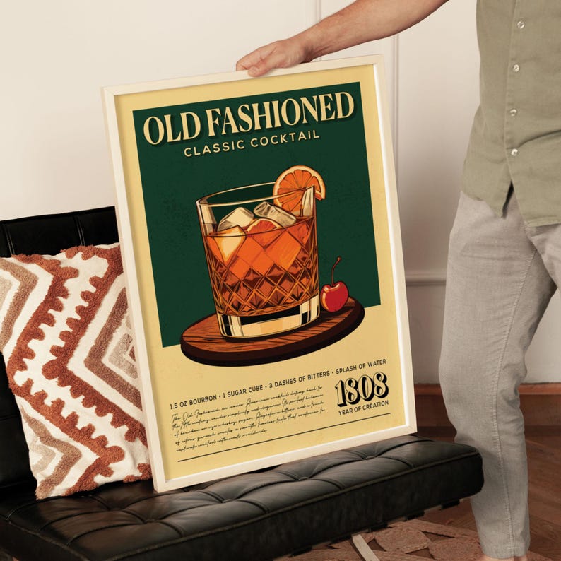 A framed poster advertising an old fashioned cocktail, featuring an illustration of a classic cocktail with a slice of orange and a cherry on a wooden coaster.