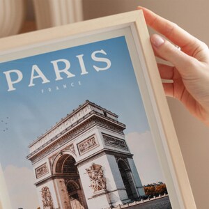 A person's hand is holding a framed picture of the Arc de Triomphe in Paris, France.