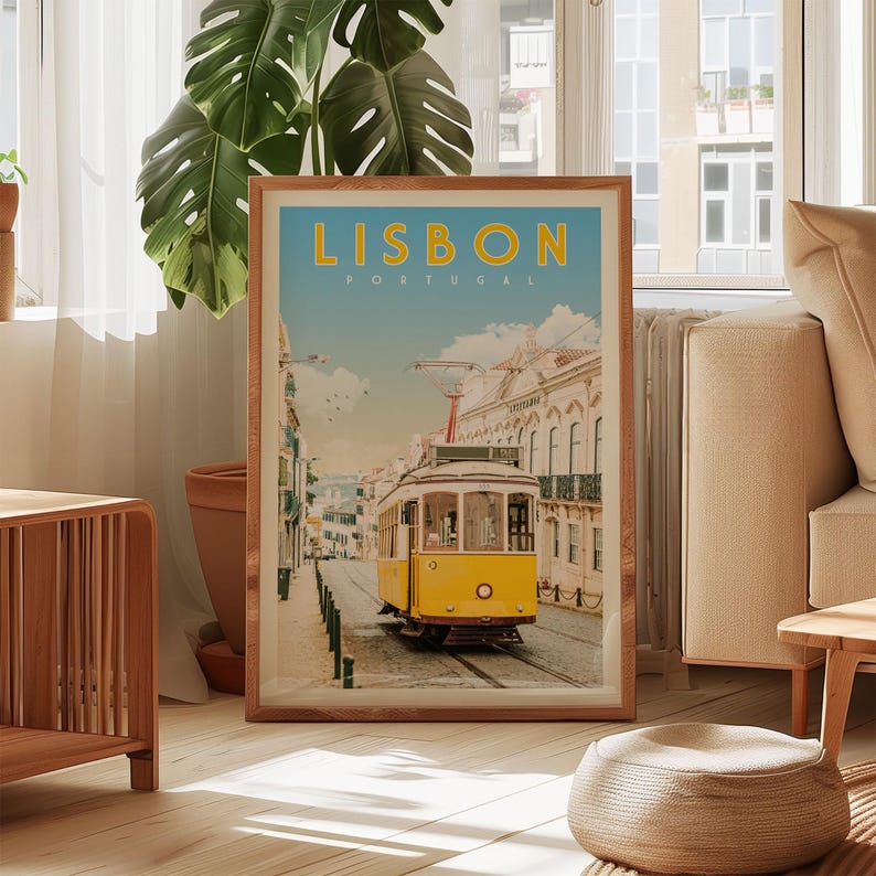 A framed poster of a yellow tram in Lisbon, Portugal, displayed in a living room with a large window and a potted plant in the background.