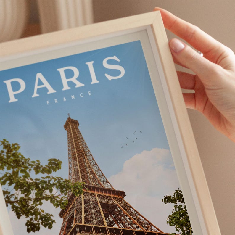 A person's hand is holding a framed picture of the Eiffel Tower in Paris, France.