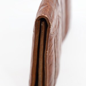 May include: A brown leather clutch bag with a textured, embossed pattern. The bag is folded over, revealing the interior layers. The leather has a worn appearance. The design is simple and classic, suitable for various occasions.