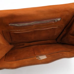 May include: Open view of a brown leather clutch bag. The interior reveals a zipped pocket and several compartments. The bag is open, showcasing its storage capacity and design. The leather has a rich, warm tone.