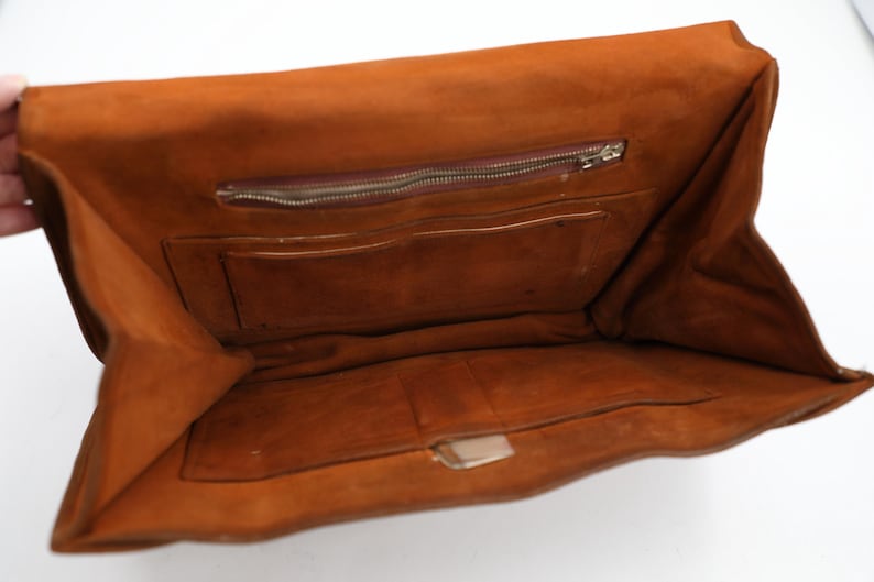May include: Open view of a brown leather clutch bag. The interior reveals a zipped pocket and several compartments. The bag is open, showcasing its storage capacity and design. The leather has a rich, warm tone.