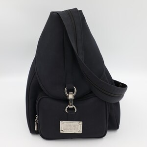 May include: A black backpack featuring a single shoulder strap, a front pocket with a silver-toned metal clasp, and a rectangular silver-toned metal plaque on the lower front section. The bag has a smooth, matte finish and a zipper closure.