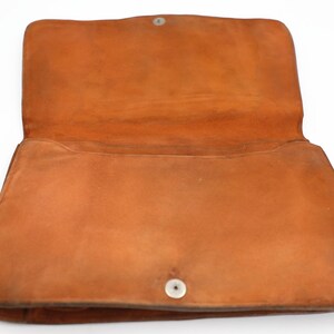 May include: An open, orange-brown leather handbag. The bag has a rectangular shape with a flap closure secured by a silver snap. The interior is visible, showing the soft, suede-like texture of the leather. The bag is likely vintage.