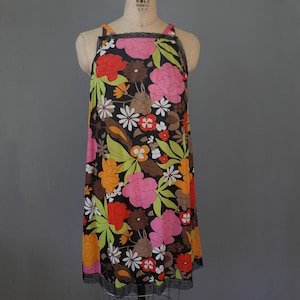 Può includere: Un abito nero senza maniche con stampa floreale con fiori rosa, arancioni, rossi e verdi. L'abito ha un bordo in pizzo sul collo e sull'orlo.