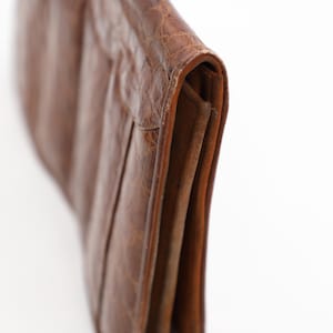 May include: A brown leather clutch bag with a textured finish. The bag is folded over, showing a section of the interior. The bag appears to be made of high-quality leather.