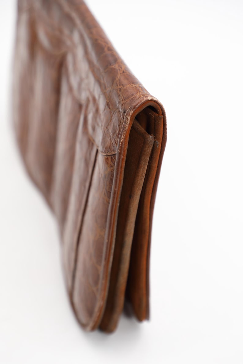 May include: A brown leather clutch bag with a textured finish. The bag is folded over, showing a section of the interior. The bag appears to be made of high-quality leather.