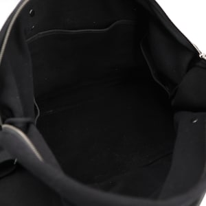 May include: A black bag with a wide open top, featuring a silver-toned metal zipper closure that runs along the upper edge. The interior is lined with black fabric and includes a flat pocket on the back wall and a snap button fastener.