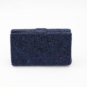Puede incluir: Un clutch rectangular azul marino con cuentas y cierre de solapa. La superficie está cubierta de pequeñas cuentas iridiscentes que crean una apariencia texturizada. Diseño simple y elegante.