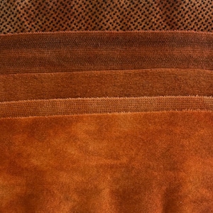 May include: Close-up of various textured fabrics in shades of brown and orange. The fabrics include a small checkered pattern, a herringbone design, and several solid, plush materials. The image showcases a range of textures and colors.