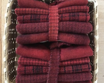 May include: Two stacks of red fabric bundles, secured with matching ribbon, are nestled in a woven basket. The fabric displays various textures and patterns, including solid and plaid designs. The basket is made of light-colored woven material.