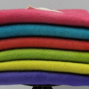 May include: A stack of six folded, colorful towels. The towels are in shades of pink, teal, red, green, yellow, and purple. The towels appear to be made of a soft, textured fabric. A small white tag is visible.