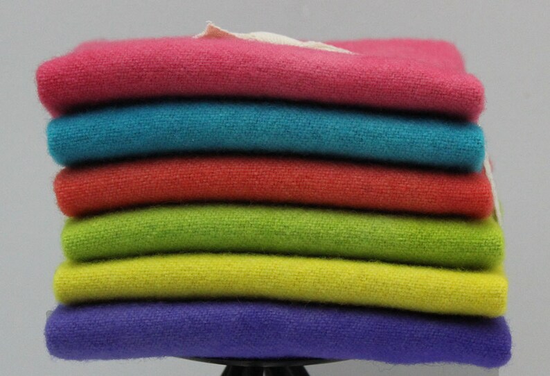 May include: A stack of six folded, colorful towels. The towels are in shades of pink, teal, red, green, yellow, and purple. The towels appear to be made of a soft, textured fabric. A small white tag is visible.