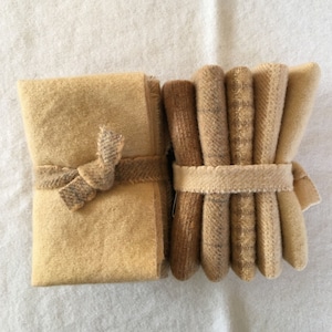 May include: Two bundles of fabric squares in shades of tan and brown. One bundle is tied with a bow, the other with a simple band. The fabrics appear to be wool or a similar material, with a textured surface.