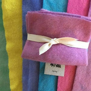 May include: A bundle of purple felt squares tied with a cream ribbon, with a small tag that reads "Spring". The felt is surrounded by colorful felt strips in shades of green, yellow, blue, pink, and purple.