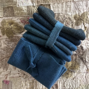 May include: A set of blue gloves and a matching scarf are displayed on a patterned surface. The gloves are a mix of solid and textured fabrics, bound together with a blue band. The scarf is folded and has a decorative bow.