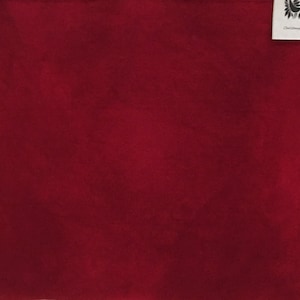May include: A solid, deep red fabric with a textured appearance. A small white tag in the upper right corner reads "Christmas Red". The fabric is likely used for crafting or home decor.