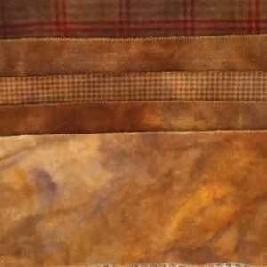 May include: Close-up of several fabric swatches in shades of brown. The top swatch has a red plaid pattern. Other swatches include solid brown, houndstooth, and a mottled, textured design. The fabrics appear to be wool or a similar material.