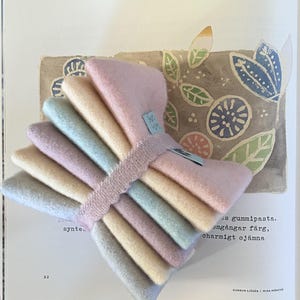 May include: A stack of pastel-colored fabric squares, including pink, yellow, blue, and lavender, bound together with a light pink ribbon. The fabric has a soft, textured appearance. The image is on a page with text and illustrations.