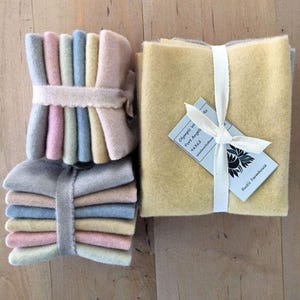May include: Stacks of pastel-colored felt squares, bundled with ribbons. One stack is wrapped with a scalloped ribbon. Another stack is wrapped with a plain ribbon. A larger bundle of yellow felt squares is tied with a white ribbon and a tag.