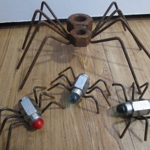 May include: Four metal spiders made from nuts and bolts. The largest spider has a double nut body and eight legs. The three smaller spiders have single nut bodies and eight legs. Each spider has a different colored glass eye.