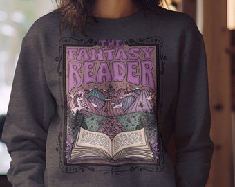 Op de afbeelding: Een donkergrijs sweatshirt met een grafisch ontwerp van een boek met een kasteel en bergen op de achtergrond. De tekst "The Fantasy Reader" is in paars op het boek gedrukt.