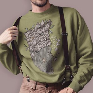 Puede incluir: Una sudadera verde con un gráfico de un árbol con una cara y el texto "Always find your way back to the forest". La sudadera la lleva una persona con cabello castaño y barba. La persona lleva tirantes marrones.