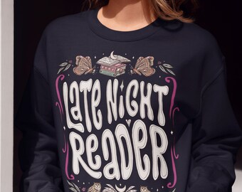 Op de afbeelding: Een marineblauw sweatshirt met een wit grafisch ontwerp dat "Late Night Reader" zegt met illustraties van uilen, vlinders en boeken.