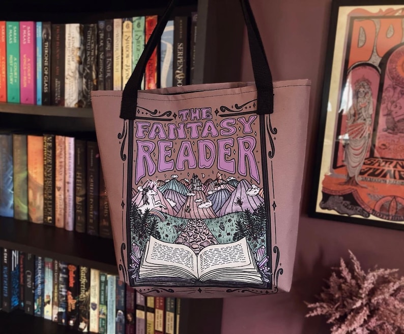 Puede incluir: Una bolsa de tela de color morado con una ilustraci&oacute;n caprichosa de un libro, un castillo y un unicornio. El texto "The Fantasy Reader" est&aacute; impreso en una fuente decorativa.