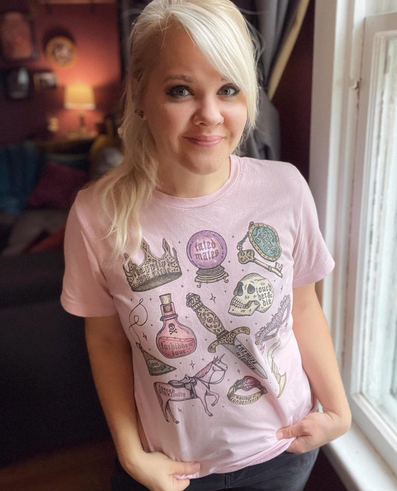 K&ouml;nnte beinhalten: Ein pinkfarbenes T-Shirt mit einem grafischen Druck verschiedener magischer Gegenst&auml;nde, darunter eine Krone, eine Zaubertrankflasche, ein Dolch, ein Sch&auml;del, eine Kristallkugel, ein Schl&uuml;ssel und ein Einhorn. Der Text auf dem Shirt lautet "failed makes".
