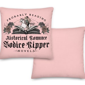 May include: A pink pillow featuring the text "Probably Reading Historical Romance Bodice Ripper Novels" and an illustration of a person riding a unicorn over an open book with roses on either side.