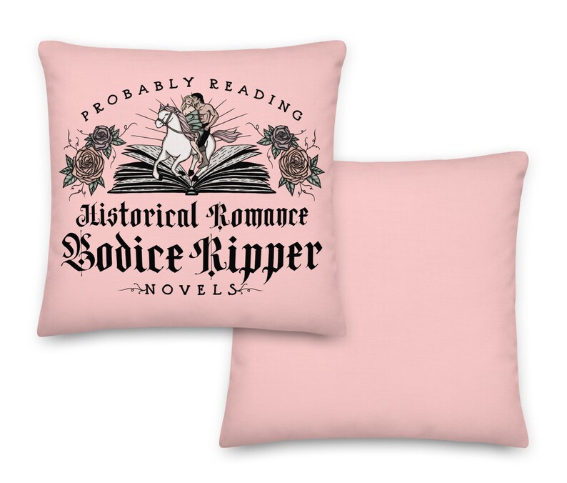 May include: A pink pillow featuring the text "Probably Reading Historical Romance Bodice Ripper Novels" and an illustration of a person riding a unicorn over an open book with roses on either side.