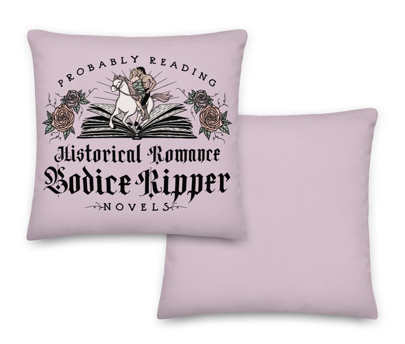 May include: A pink throw pillow with a black and white graphic design. The graphic features a couple riding a horse on top of an open book. The text reads "Probably Reading Historical Romance Bodice Ripper Novels".