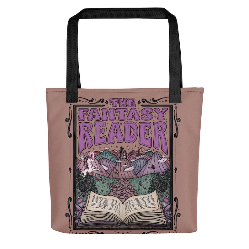 Puede incluir: Una bolsa de tela marr&oacute;n con asas negras presenta una ilustraci&oacute;n de estilo vintage de un libro, un unicornio y un castillo. El texto "THE FANTASY READER" est&aacute; impreso en letras moradas.