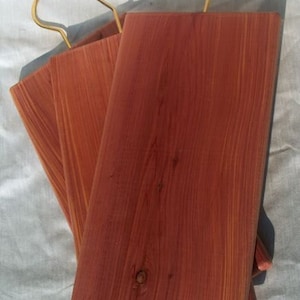 May include: Three cedar wood hangers with gold metal hooks. The hangers are stacked on top of each other.