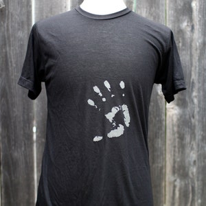 Pode incluir: Uma camiseta preta com um design de impressão de mão branca na frente.