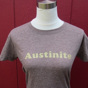 May include: A brown t-shirt with the word "Austinite" printed in yellow on the front.
