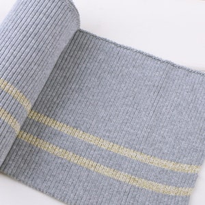 May include: Gray ribbed knit fabric with two gold stripes. The fabric is rolled up and the stripes are visible on the top and bottom of the roll.