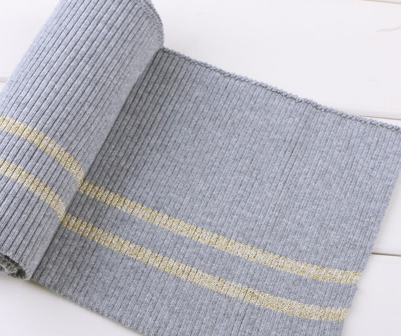 May include: Gray ribbed knit fabric with two gold stripes. The fabric is rolled up and the stripes are visible on the top and bottom of the roll.