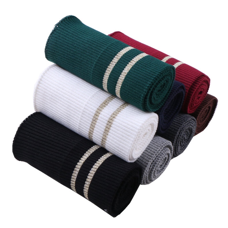 May include: A stack of rolled knit fabric with gold stripes. The fabric is in various colors including green, white, black, gray, navy, burgundy, and brown.