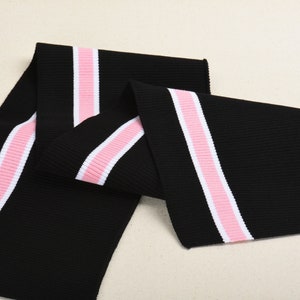 Op de afbeelding: Zwarte geribbelde brei met twee roze en witte strepen. Deze stof wordt vaak gebruikt voor manchetten en kragen.