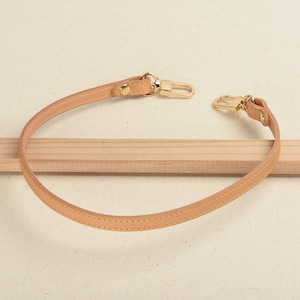 Puede incluir: Una correa de cuero marrón claro con herrajes dorados y costuras amarillas. La correa mide aproximadamente 76 cm de largo y tiene un gancho en cada extremo.