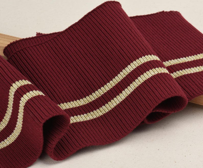 May include: Burgundy ribbed knit fabric with two gold stripes. This fabric is perfect for adding a touch of elegance to any project.