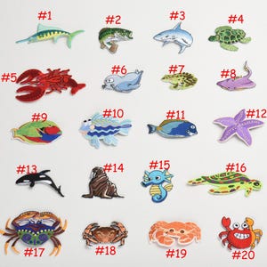 Puede incluir: Veinte parches bordados de colores para planchar que representan varias criaturas marinas, incluyendo un pez, un cangrejo, una tortuga, una estrella de mar, un caballito de mar y una ballena. Los parches están numerados del 1 al 20.