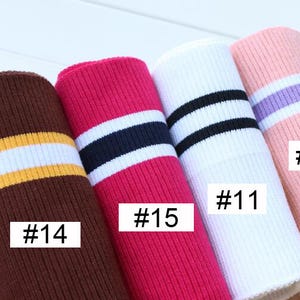Op de afbeelding: Vijf verschillende soorten geribbelde breisels met contrasterende strepen. De stof is bruin met gele en witte strepen, roze met zwarte en witte strepen, wit met zwarte strepen, roze met paarse strepen en bruin met witte strepen. De stof is gemarkeerd met de nummers #10, #11, #14, #15 en #14.