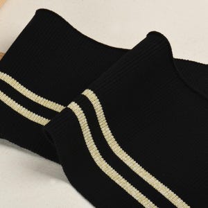 May include: Black ribbed knit fabric with two gold stripes. This fabric is perfect for adding a sporty touch to clothing.