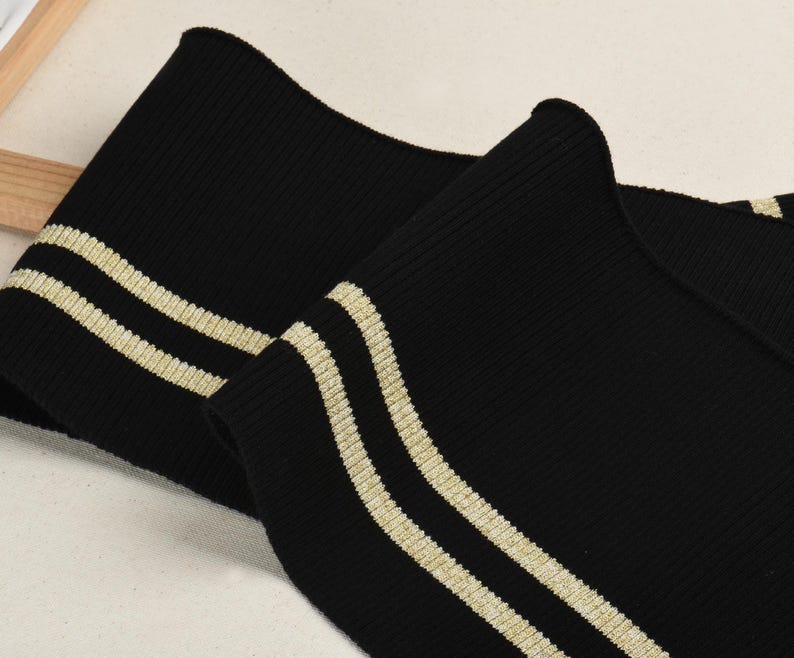 May include: Black ribbed knit fabric with two gold stripes. This fabric is perfect for adding a sporty touch to clothing.
