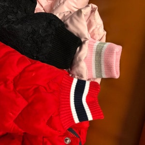 Op de afbeelding: Drie verschillende jasmanchetten met verschillende gekleurde strepen. De eerste manchet is zwart met een witte streep, de tweede manchet is roze met een witte en grijze streep, en de derde manchet is rood met een witte en marineblauwe streep.